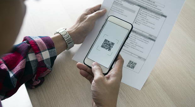 A man uses a smartphone to scan the QR code to pay monthly credit card bills after receiving an invoice sent to home. Online bill payment concept